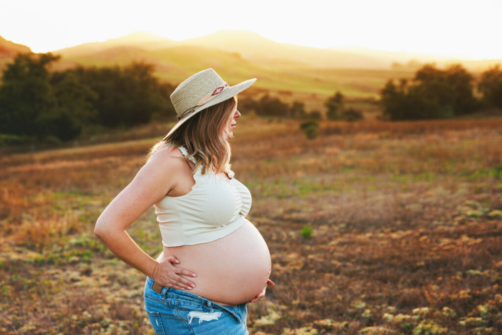 a pregnant woman wearing a hat standing in a field